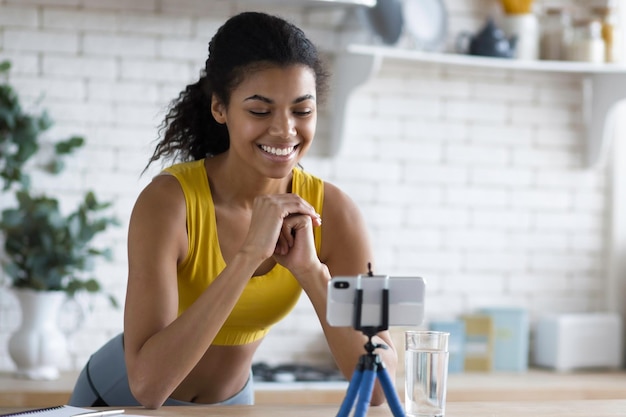 Photo handsome  african american woman fitness vlogger record streaming video about fitness and a healthy lifestyle at home in the kitchen, young female blogger shoot social media vlog on smartphone