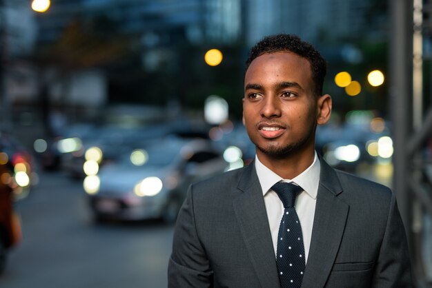 Handsome African businessman outdoors at night smiling and thinking