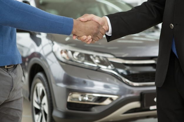 Foto uomo africano bello che stringe le mani con il commerciante di automobile dopo l'acquisto di un'auto