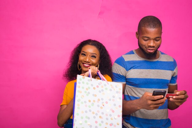 handsome african man shopping for his friend online while she holds shopping bags on her hand.