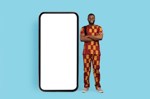 Handsome african man in traditional costume standing next to big blank smartphone