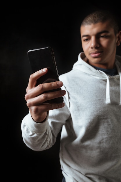 Foto atleta africano bello del giovane in maglia con cappuccio facendo uso del telefono cellulare