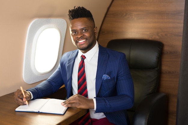 Красивый африканский молодой человек в костюме в кабине частного самолета