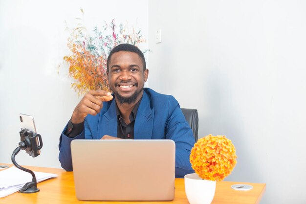 Красивый афро-американский бизнесмен в классическом костюме использует ноутбук и улыбается, работая в офисе