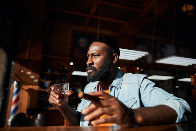 Handsome Afro American man smoking cigar and drinking whisky