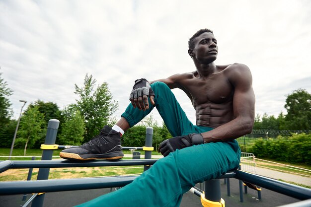 Handsome afro American sportman sitting on the street while taking break after training Black male having rest after workout