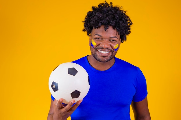 Красивый афро-бразилец Бразильский болельщик ЧМ-2022 рука об руку поет национальный гимн Бразильская музыка любимая родина патриот Бразильский болельщик держит футбольный мяч