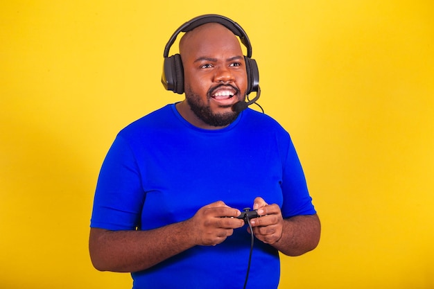 Handsome afro brazilian man wearing glasses blue shirt over\
yellow background playing with friends multplayer gamer interacting\
voice call games entertainment
