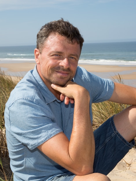Фото Красивый и уверенный в себе человек улыбается и сидит на пляже