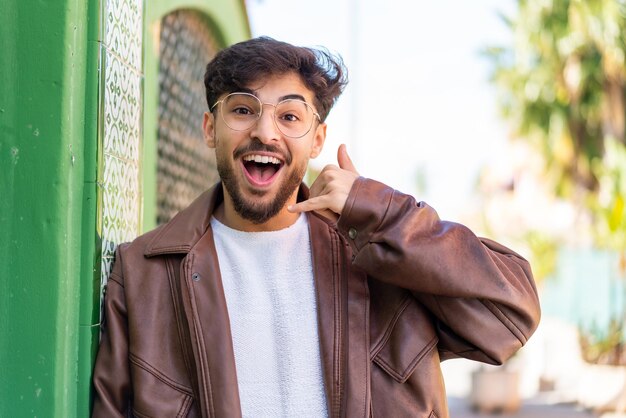 Handsome arab man at outdoors making phone gesture call me back sign