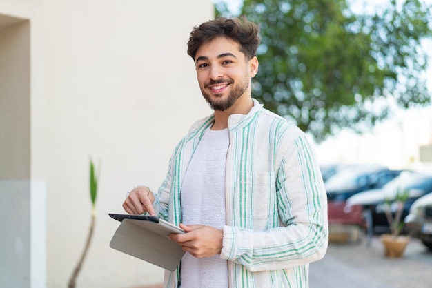 Foto bell'uomo arabo all'aperto che tocca lo schermo del tablet con un'espressione felice