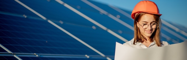 Handsome Architect Woman Examining a Draft Map or Blueprint Project Plan, Worker Activity Looking Out in Photovoltaic Cell Farm or Solar Panels Field.