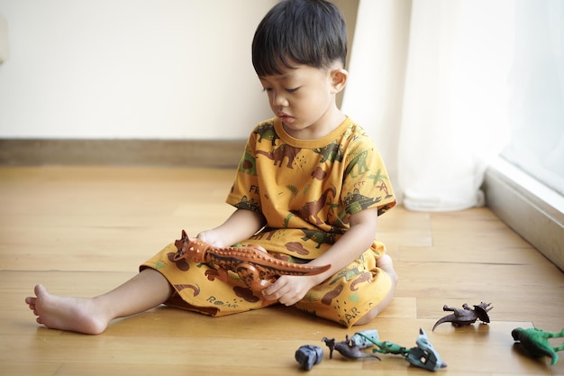 Handsome asian boy toddler boy playing with plastic dinosaur toy at home soft back light