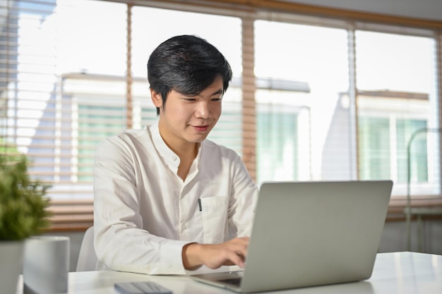 Handsome Asian businessman or male office worker using his laptop at his desk