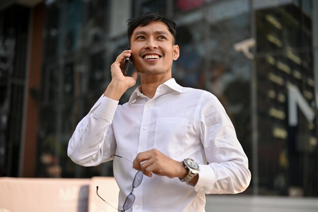 Handsome Asian businessman talking on the phone with his business partner while walking in a city