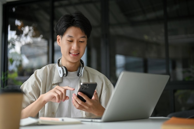 Handsome Asian male college student using his smartphone at the table in the coffee shop