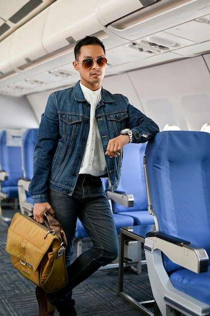 Handsome Asian male traveler stands at the aisle carrying his luggage tourist traveler passenger