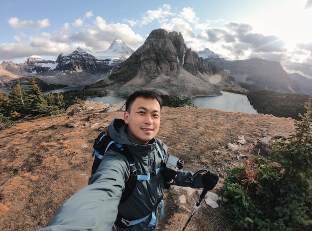 Handsome asian male traveler taking selfie portrait on the hill with mount assiniboine in national park at BC Canada