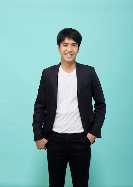 Handsome Asian man in a black suit looking at camera on light blue studio isolated background