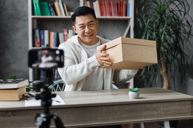 선물 상자를 풀면서 카메라에 비디오를 녹화하는 평상복 차림의 잘생긴 아시아 남자