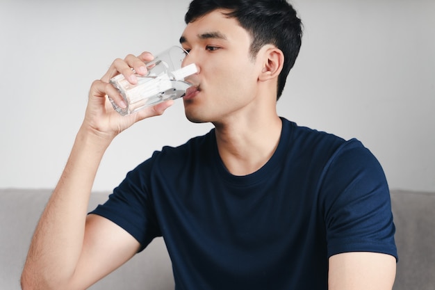 居間のソファで水を飲むハンサムなアジア人男性