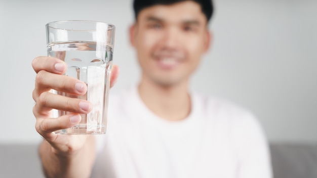 居間のソファで水を飲むハンサムなアジア人男性