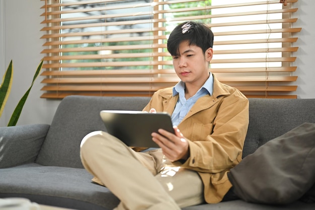 집에서 디지털 태블릿으로 온라인으로 작업하는 소셜 네트워크에서 의사소통하는 잘생긴 아시아 남자 프리랜서