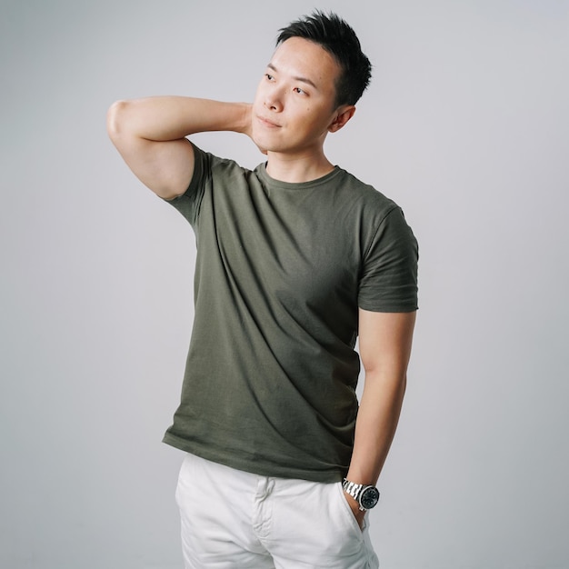 handsome asian man green tshirt touching neck standing isolated gray wall