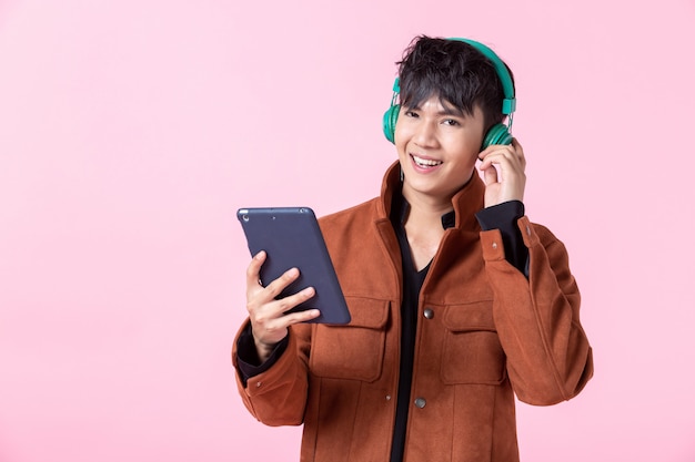 Handsome asian man listening to music on pink background