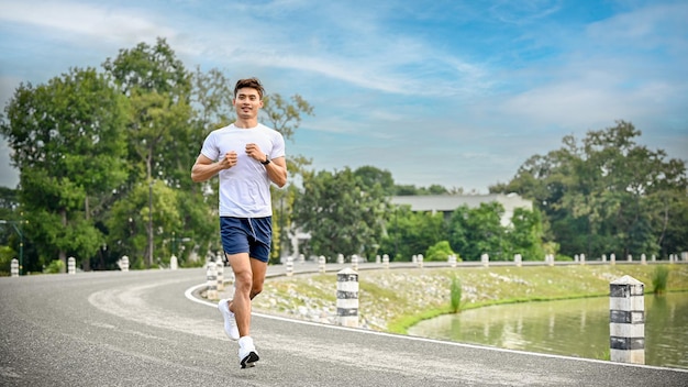 Handsome Asian man running or jogging on the side path along the beautiful lake