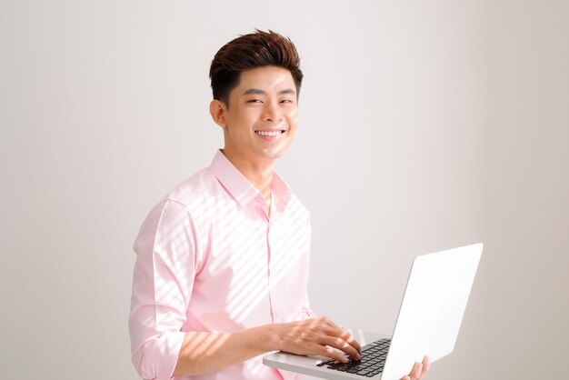 Bell'uomo asiatico in piedi con il computer portatile su sfondo grigio