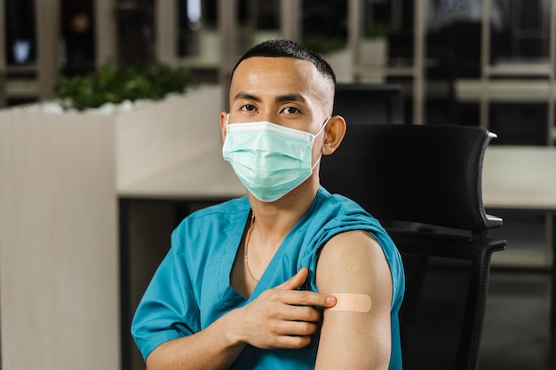 Handsome asian man vaccinated against coronavarus and showing patch on his arm Covid19 vaccination Filipino man in medical mask