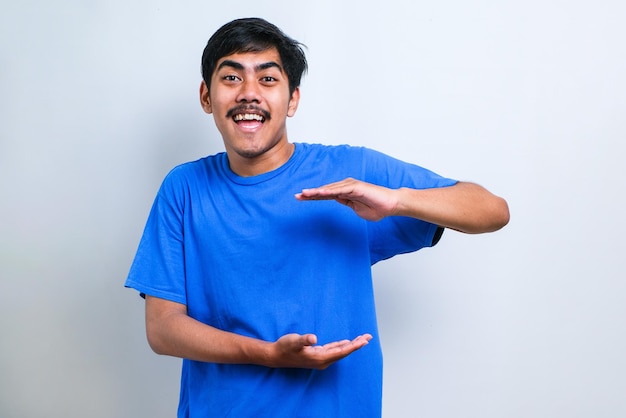 Handsome asian man wearing casual t-shirt over white background gesturing with hands showing big and large size sign, measure symbol. smiling looking at the camera. measuring concept.