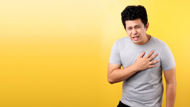 Handsome Asian man with heart pain,on yellow wall.