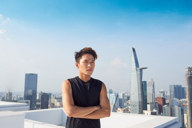 Bell'uomo asiatico con abbigliamento sportivo in piedi sullo sfondo della città incrociando le braccia