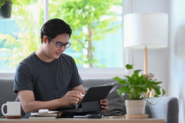 Handsome asian man working with computer tablet on sofa.