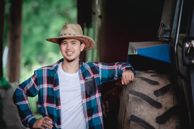 Uomini asiatici bei che indossano le camice sorridenti accanto ai trattori per gli agricoltori