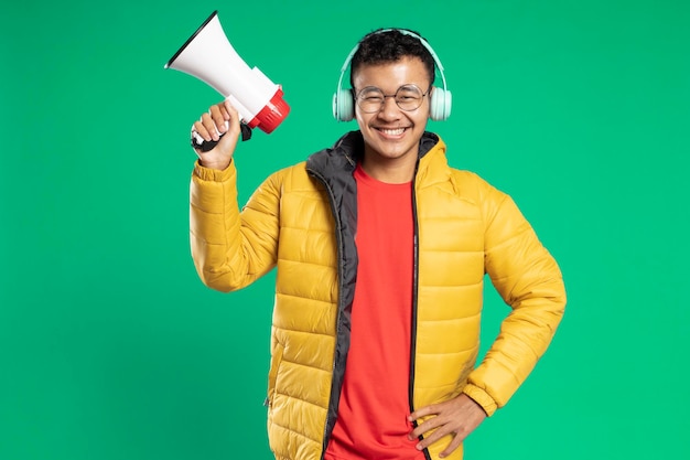 Handsome asian young man smiling holding megaphone on green background