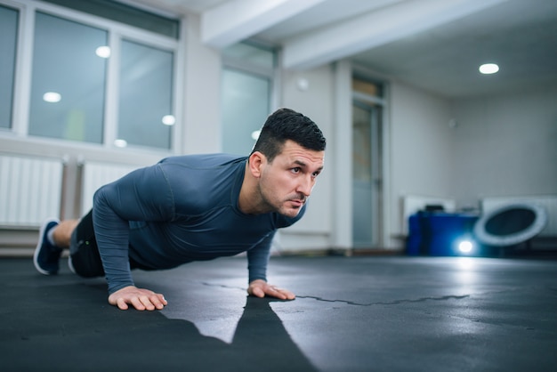 Handsome athlete doing push-ups indoors. Low angle image.