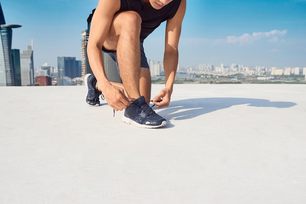 Bello atleta che si allaccia i lacci delle scarpe in una giornata di sole