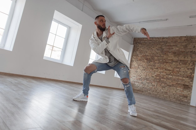 Handsome attractive dancer man in fashionable clothes with ripped jeans dancing in dance studio