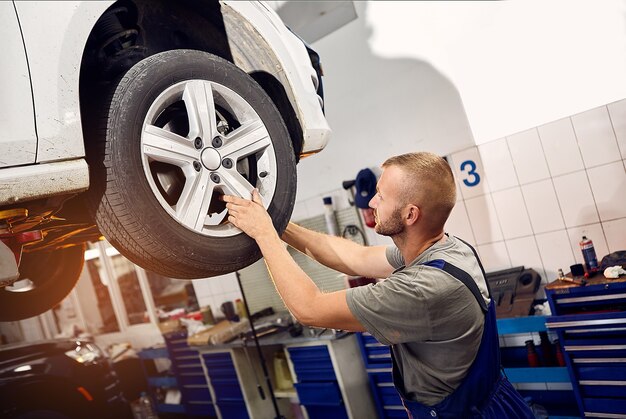 Handsome auto mechanic installs and inspects the wheels on the car.