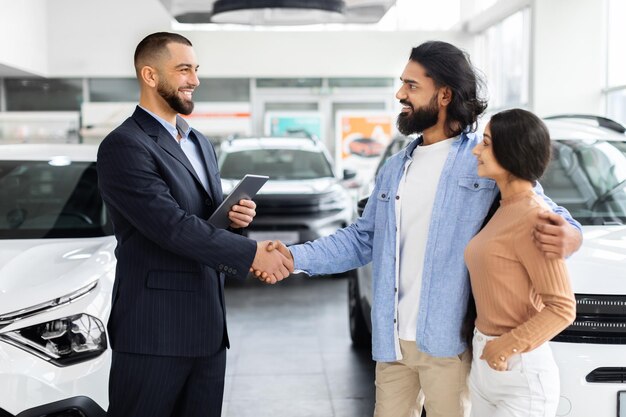 Handsome auto salesman shaking indian guy customer hand