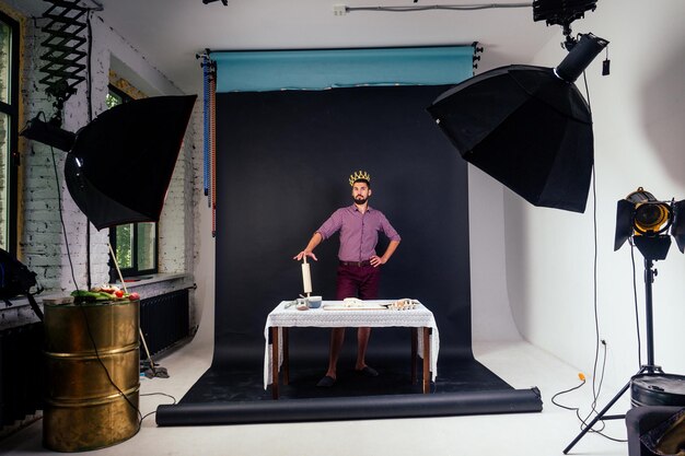 A handsome baker man with beard confectioner bakery with a golden crown on his head king of the kitchen bakes bread pizza pasta holding a rolling pin kneading dough in studio on a black background