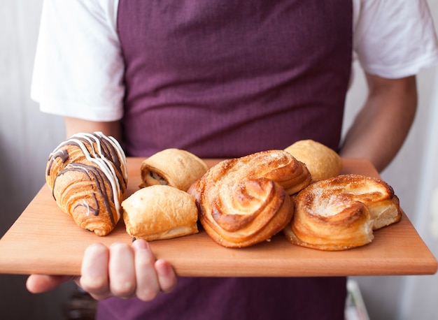 Handsome baker in uniform holding tray full of freshly baked croissants