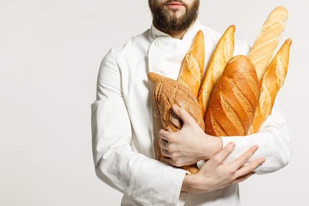 A handsome baker in uniform holds baguettes on a white background bakery advertising concept