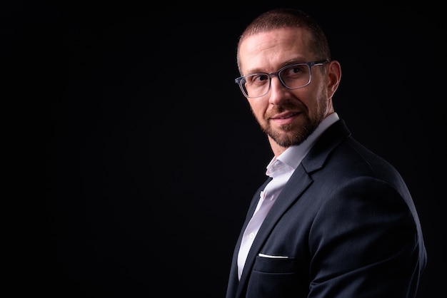 handsome bald bearded businessman in suit wearing eyeglasses against black space