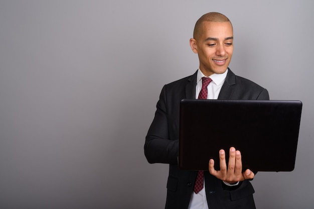 handsome bald businessman wearing suit with laptop on gray