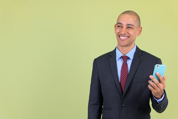 handsome bald multi ethnic businessman wearing suit against colored wall