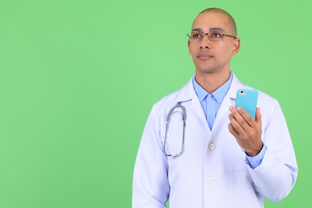  handsome bald multi ethnic man doctor against green wall